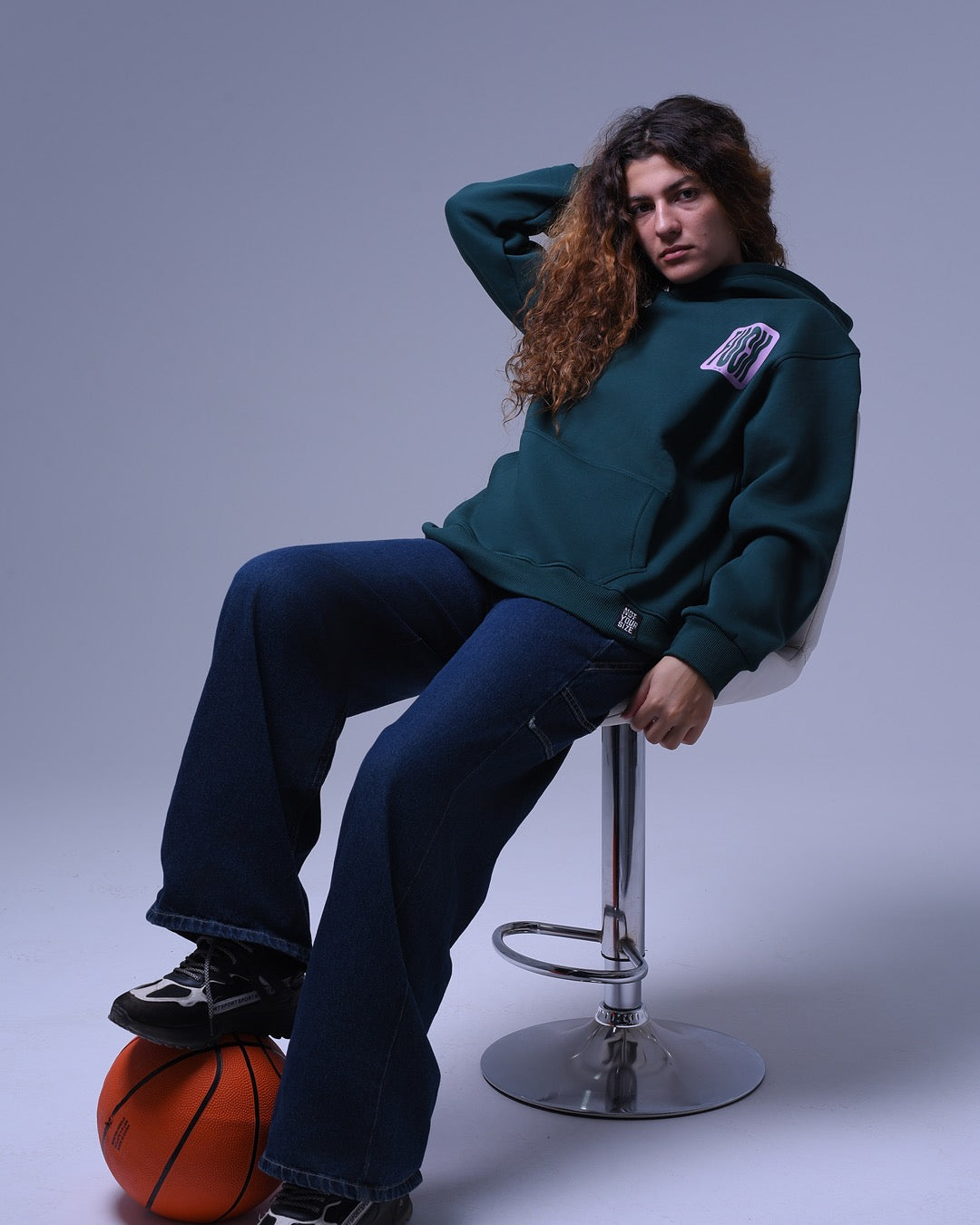Model wearing a dark green oversized hoodie for unisex by NotYourSize2025 sitting on a stool with a basketball