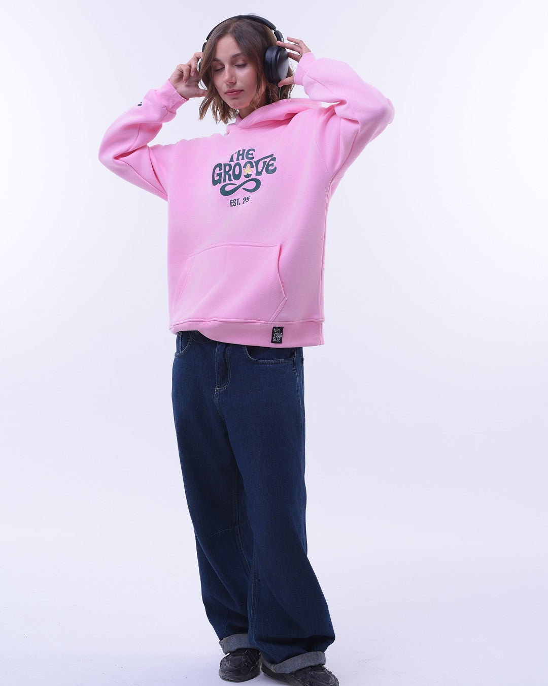 Pink oversized hoodie for women with The Groove graphic worn by model with headphones