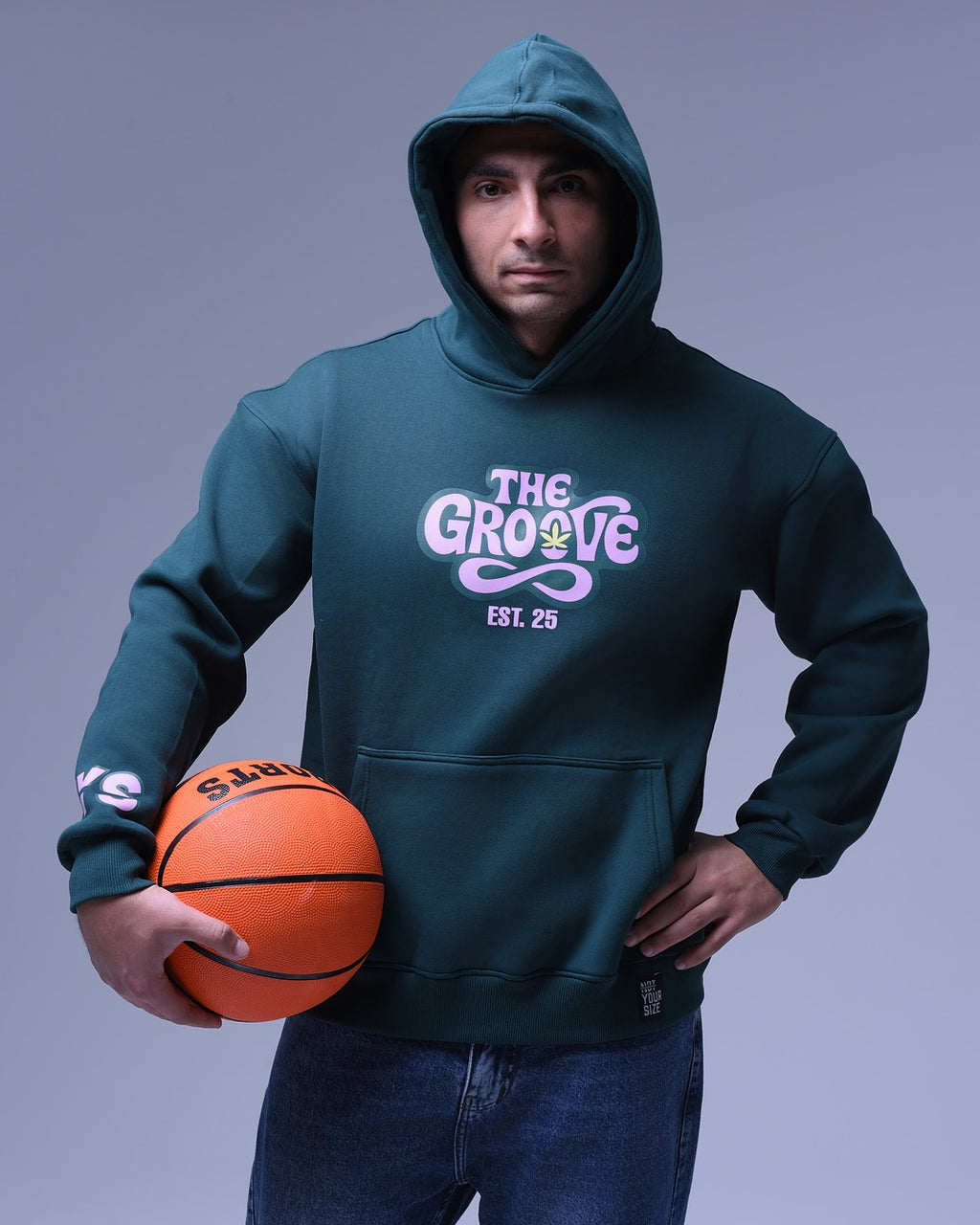 Man wearing a dark green oversized hoodie for women with The Grove logo holding a basketball
