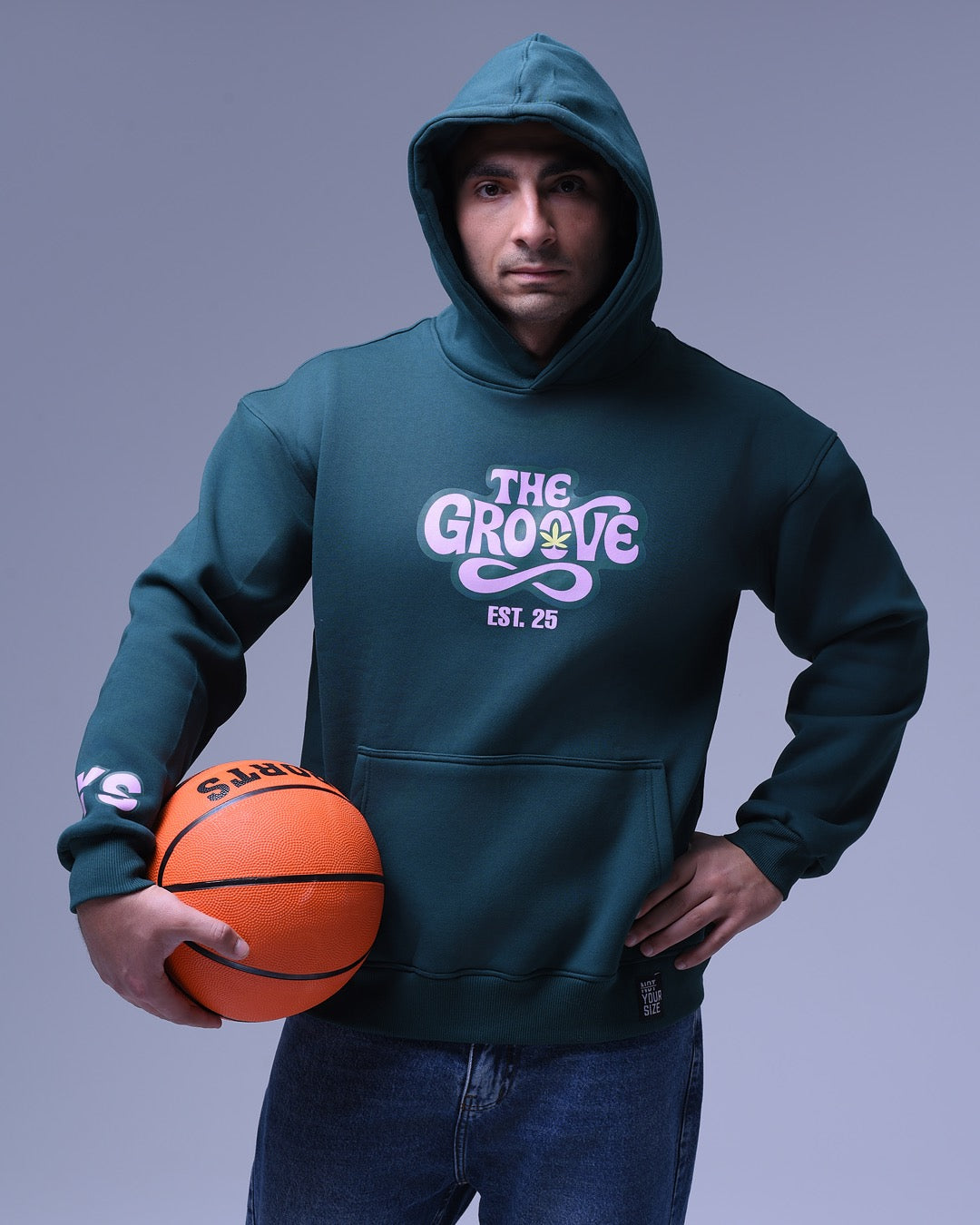 Man wearing a dark green oversized hoodie for women with The Grove logo holding a basketball
