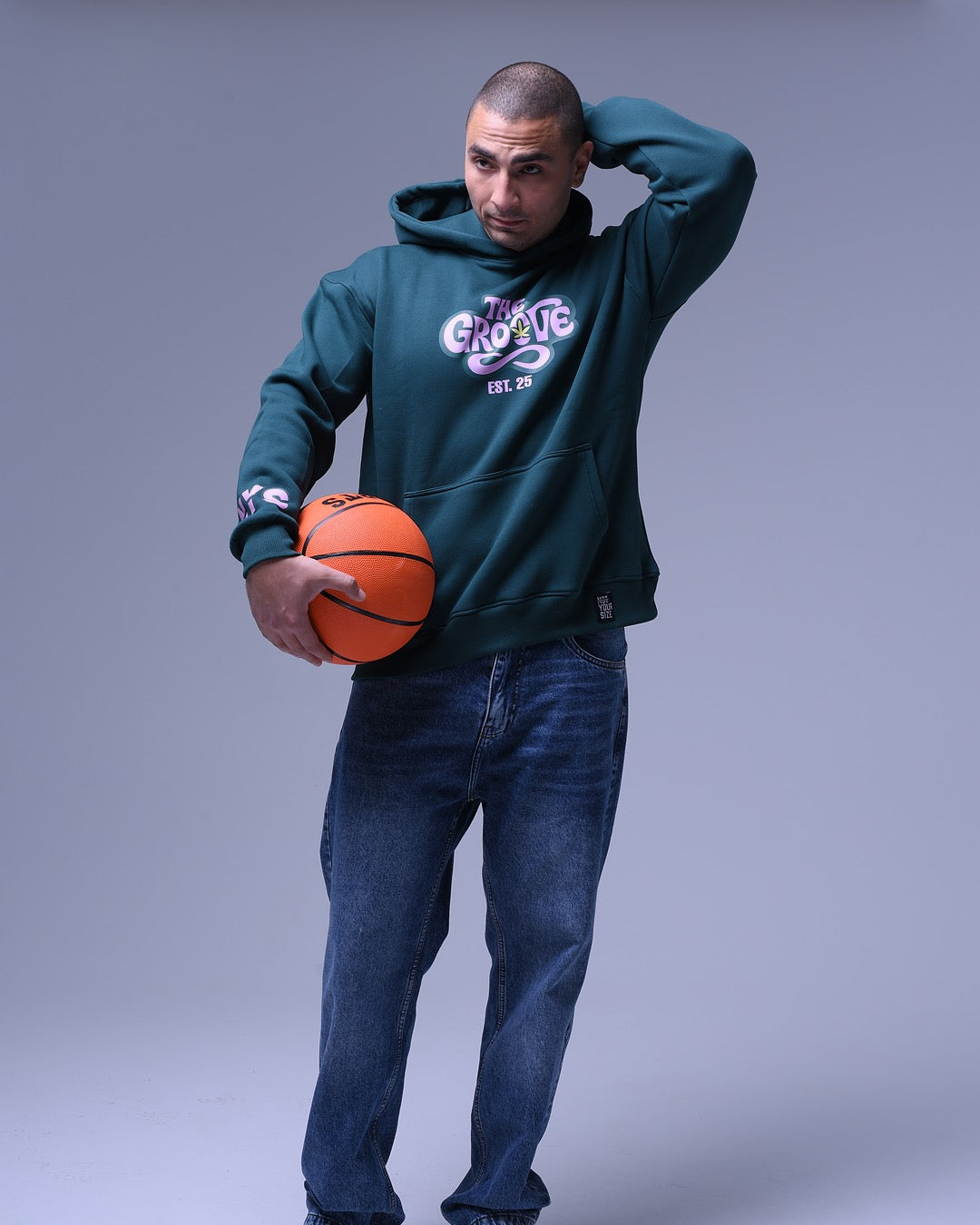 Man wearing dark green oversized hoodie for women holding a basketball against gray background