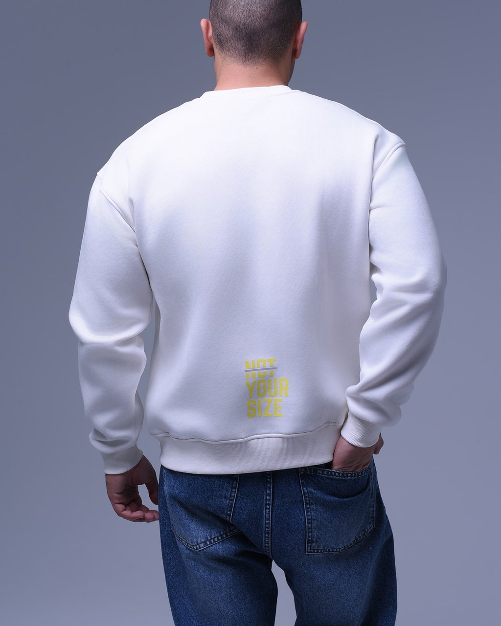 Back view of man wearing white oversized crewneck sweatshirt by NotYourSize2025 with yellow logo on lower back