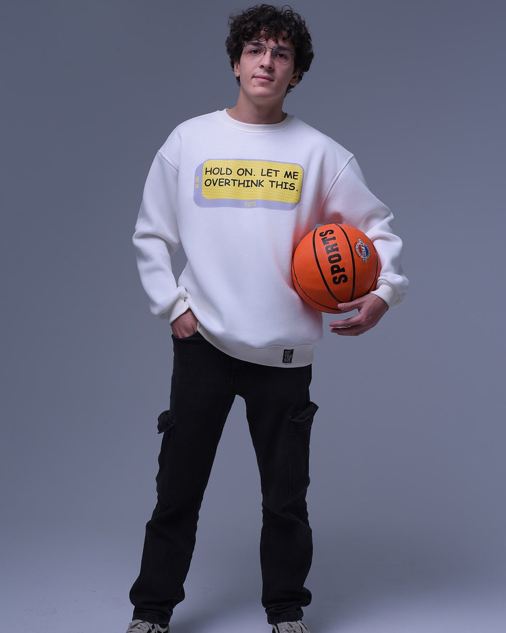 Young man wearing NotYourSize2025 oversized crewneck sweatshirt holding a basketball with text print