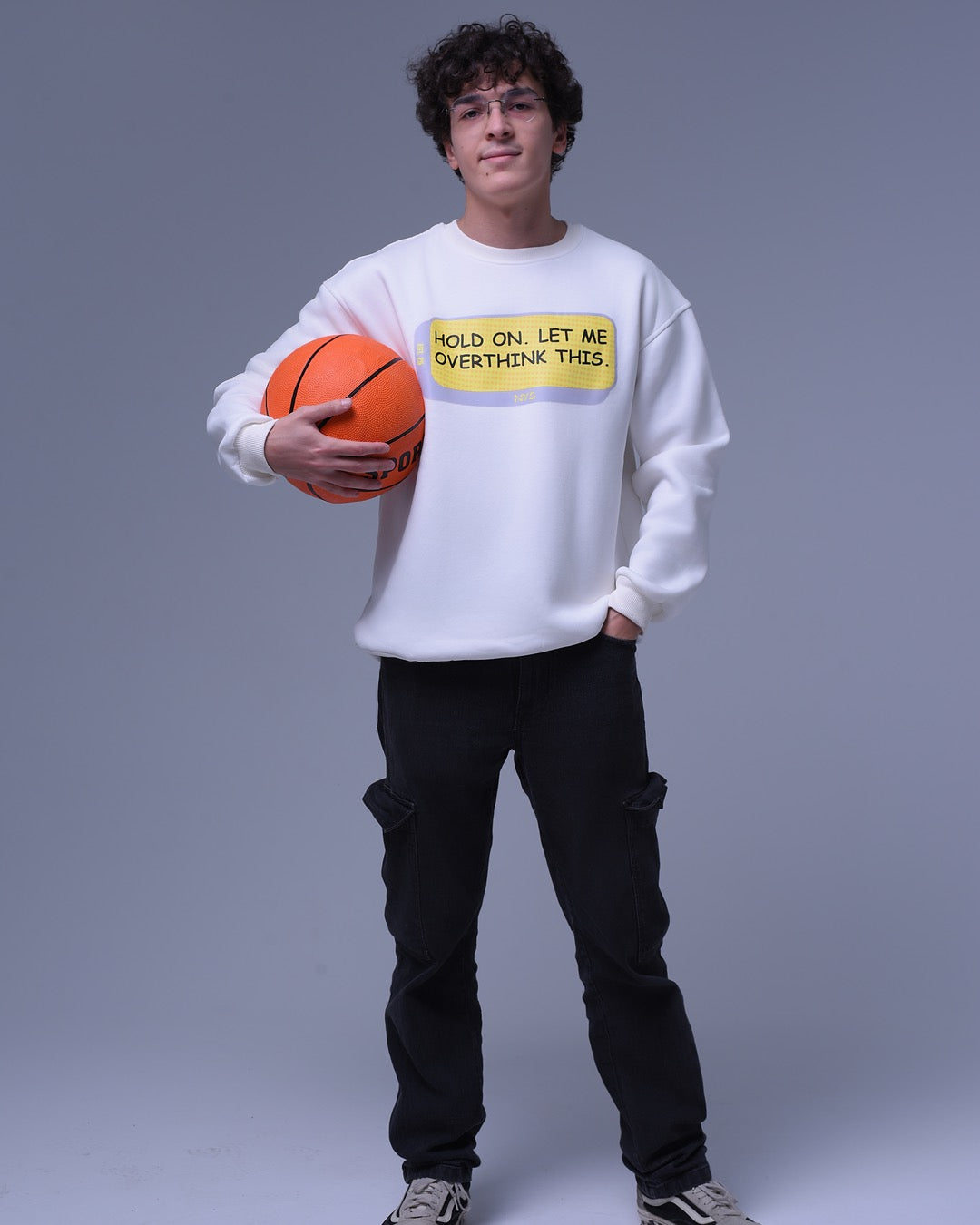 Young man wearing a white oversized crewneck sweatshirt with text holding a basketball