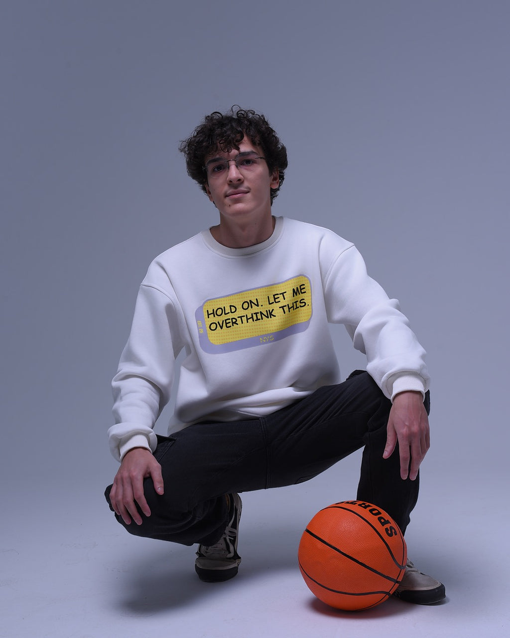 Man wearing white oversized crewneck sweatshirt with text design posing with basketball