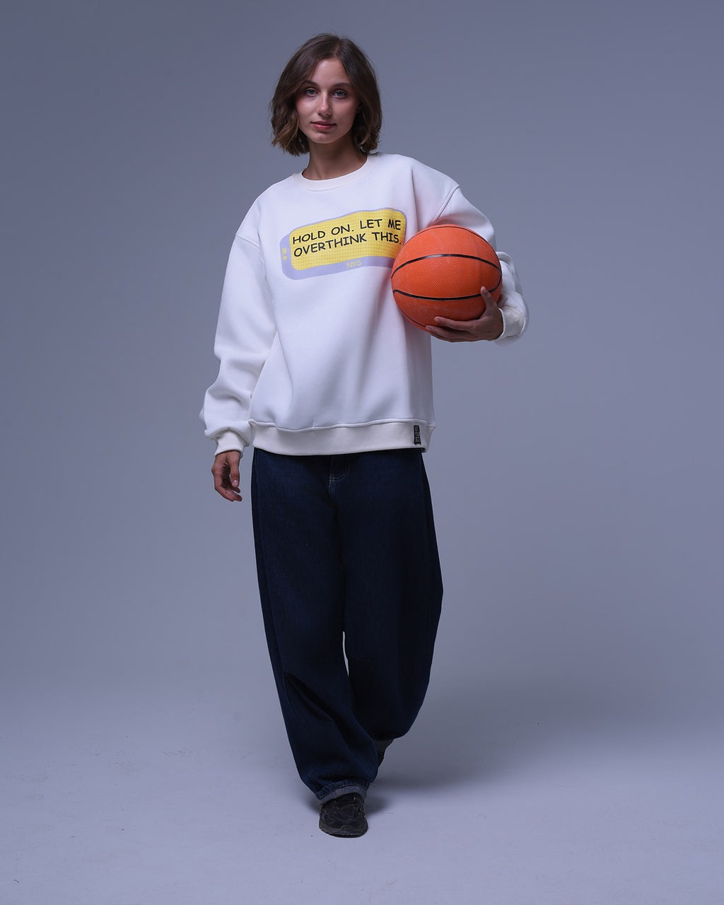 Woman wearing white oversized crewneck sweatshirt holding basketball with casual black pants