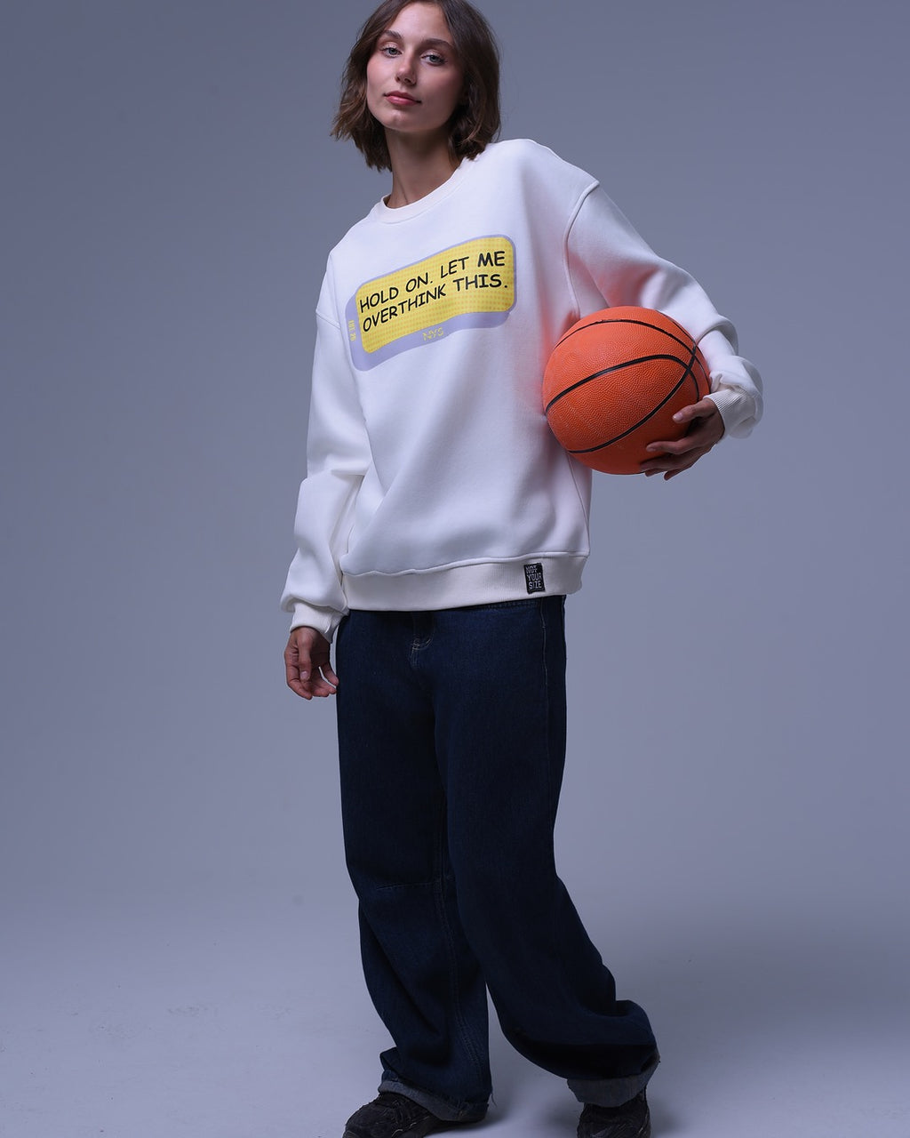 NotYourSize2025 oversized crewneck sweatshirt in white with text print worn by model holding basketball